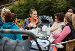 Mehrere Mütter sitzen kaffeetrinkend an einem Tisch im Freien und unterhalten sich | © SolStock - Getty Images